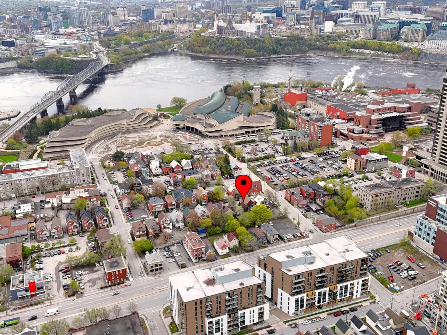 Aerial view of an Ottawa neighborhood with a red map pin marking a property near the river and Parliament Hill.