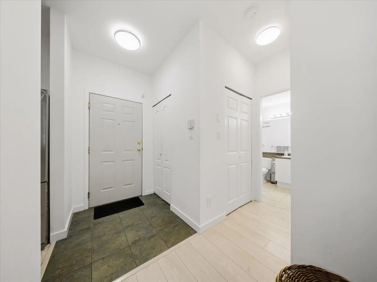 Bright, white entryway with a front door, closet, and bathroom visible. The floor transitions from tile to wood.