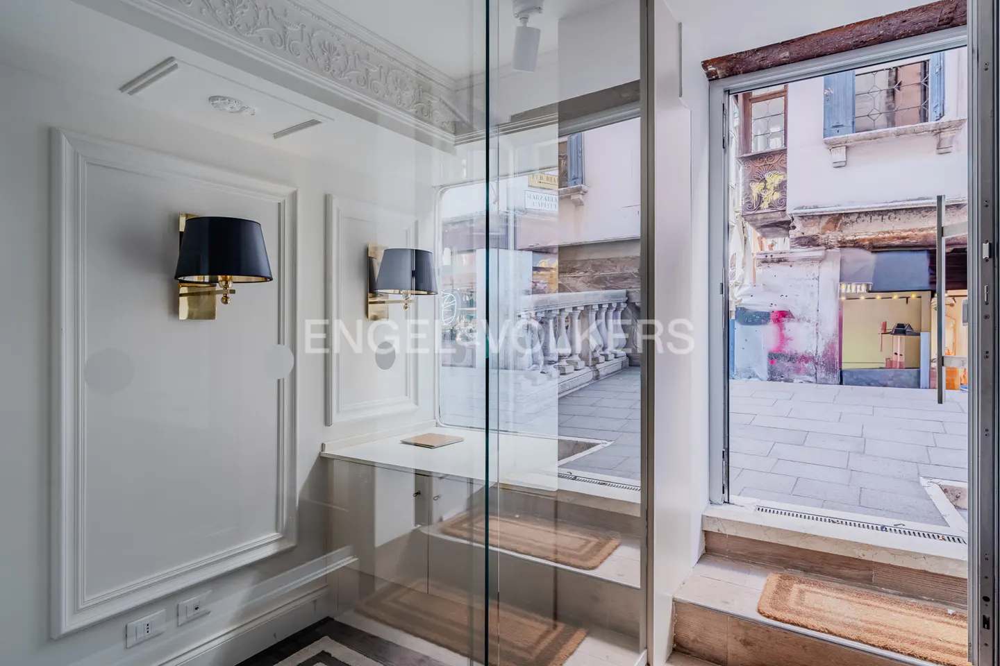 Interior view of a Venice apartment entrance with black lamps, marble floors, and a view of a Venetian street.