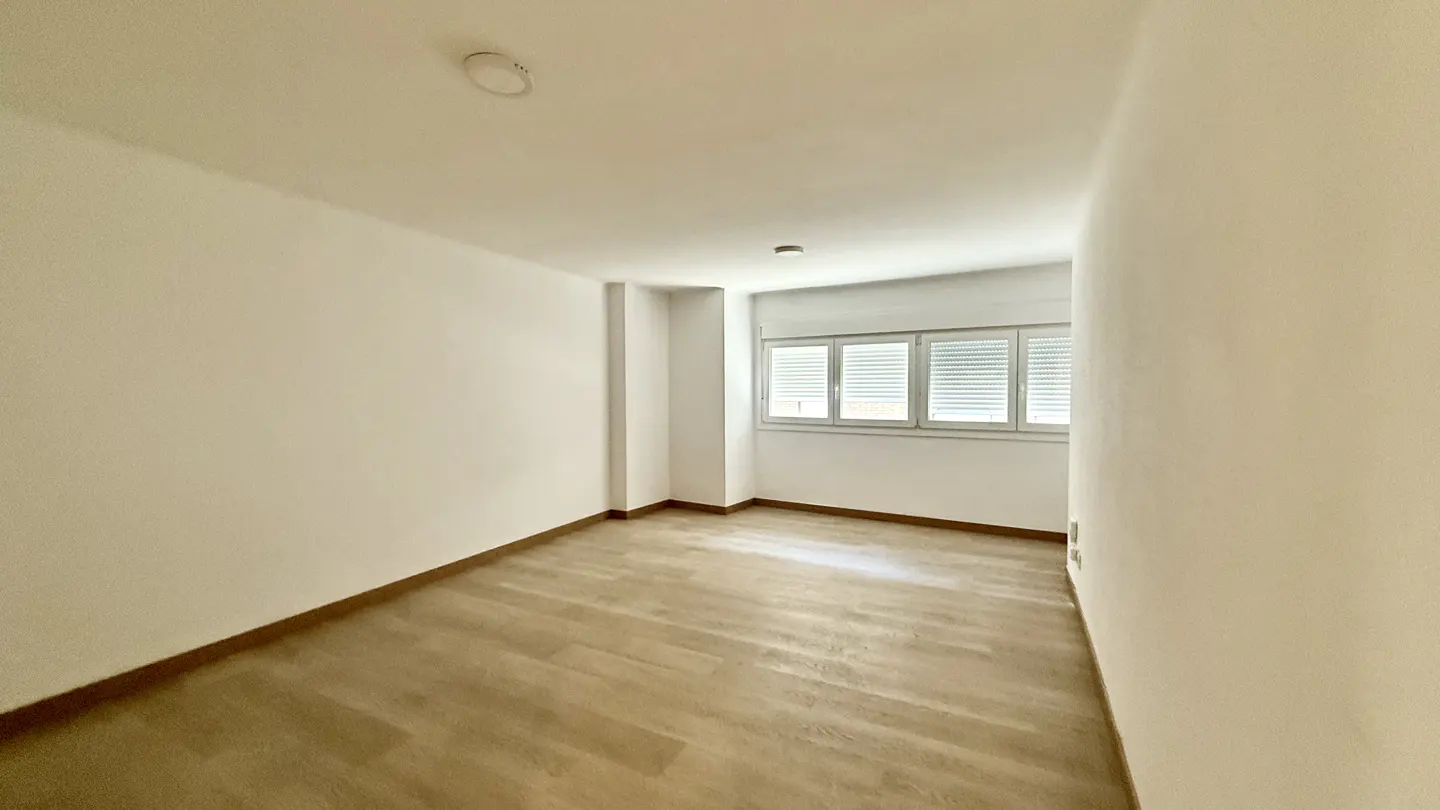Empty room with light wood floors, white walls, and a window with white blinds.