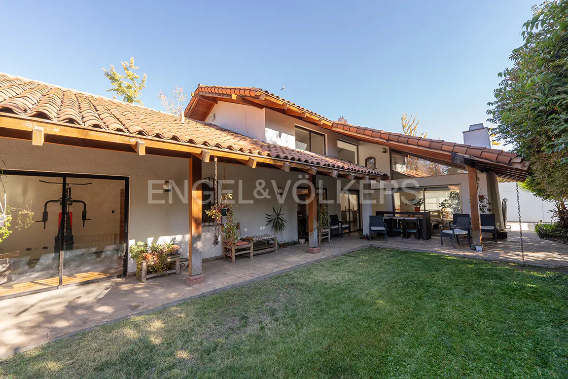 Exterior view of a house with a red tile roof, a covered patio with seating, and a green lawn.