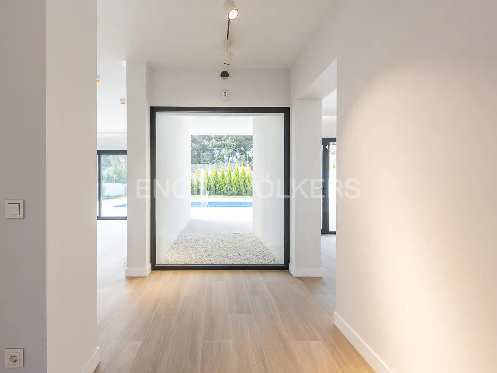 Hallway with light wood floors and white walls leads to a pool view through a black-framed opening. Track lighting on the ceiling.