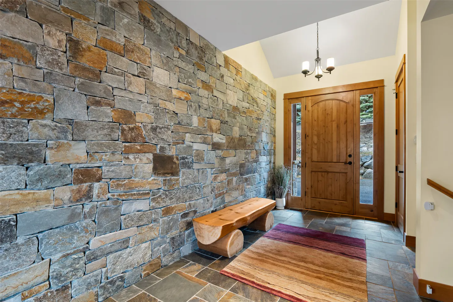 Foyer with stone wall, wood bench, and rug. A wood door with glass panels is centered. A chandelier hangs from the ceiling.