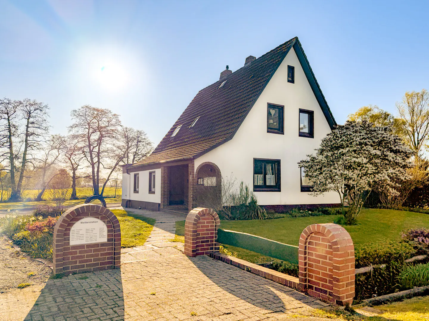 Two-story white house with a brown roof, green lawn, and brick walkway under a sunny blue sky.