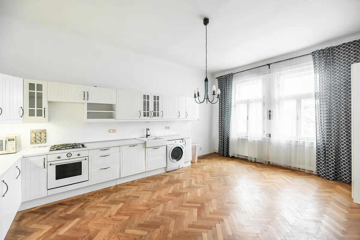 Bright kitchen with white cabinets, herringbone wood floors, a modern chandelier, and windows with patterned curtains.