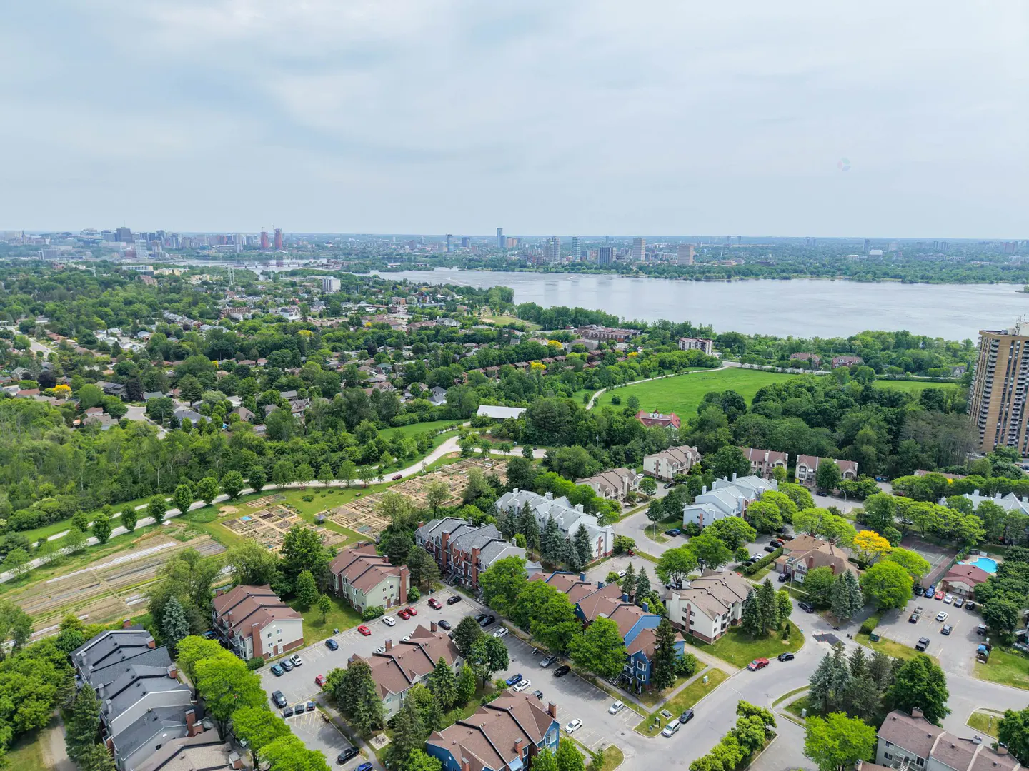 Aerial view of a suburban neighborhood with multi-story apartment buildings, green trees, and a distant city skyline.