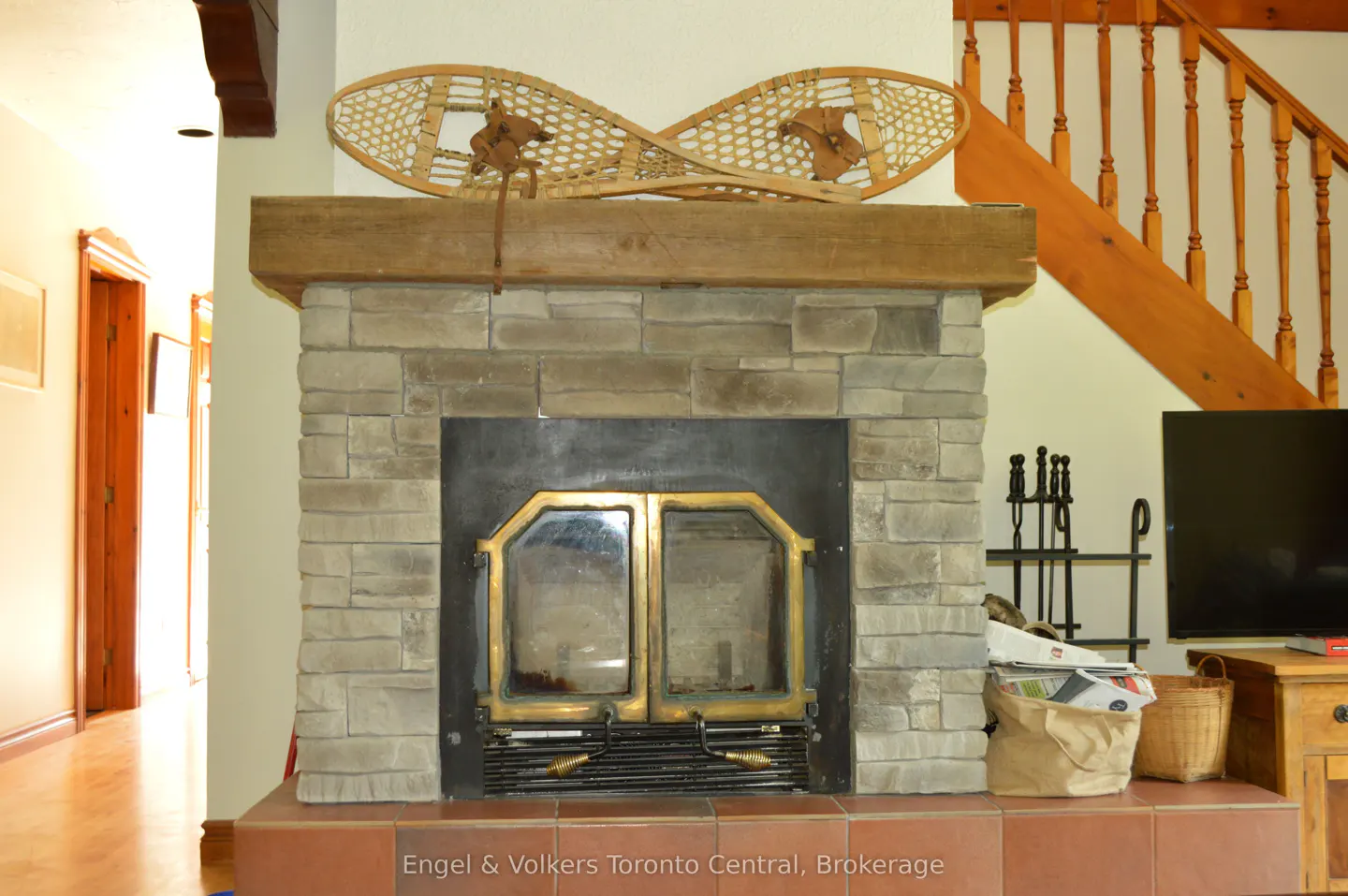 Stone fireplace with a wooden mantel and snowshoes on top. A staircase is visible in the background.