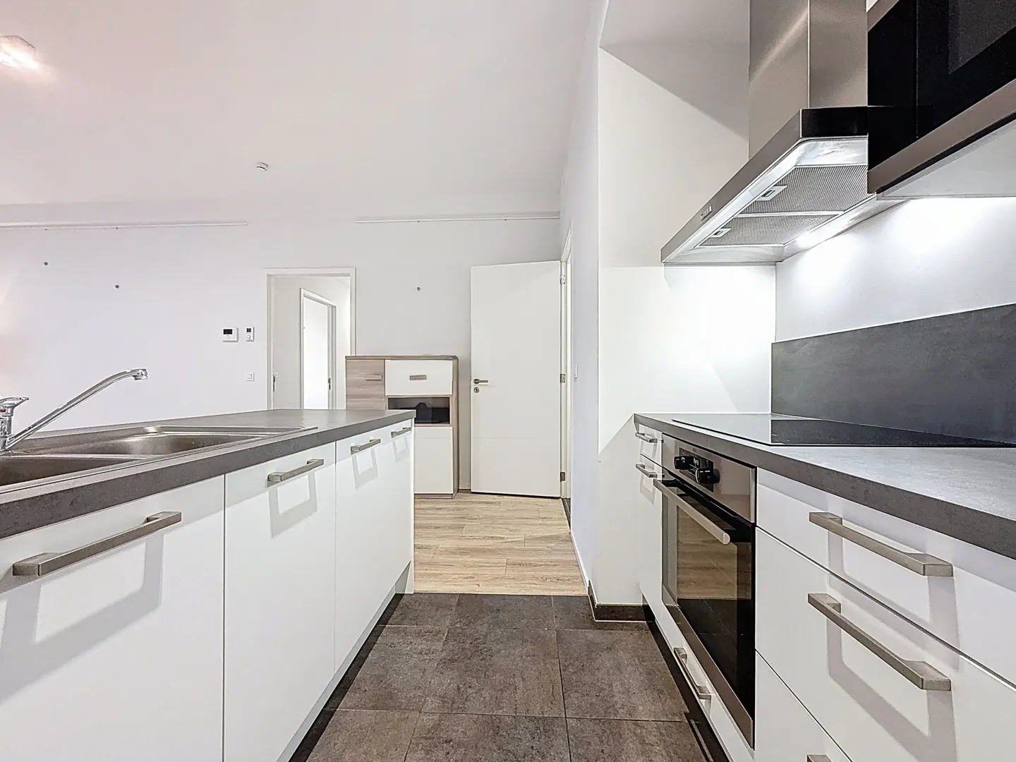 Modern kitchen with white cabinets, dark grey countertops, stainless steel appliances, and dark tile flooring.