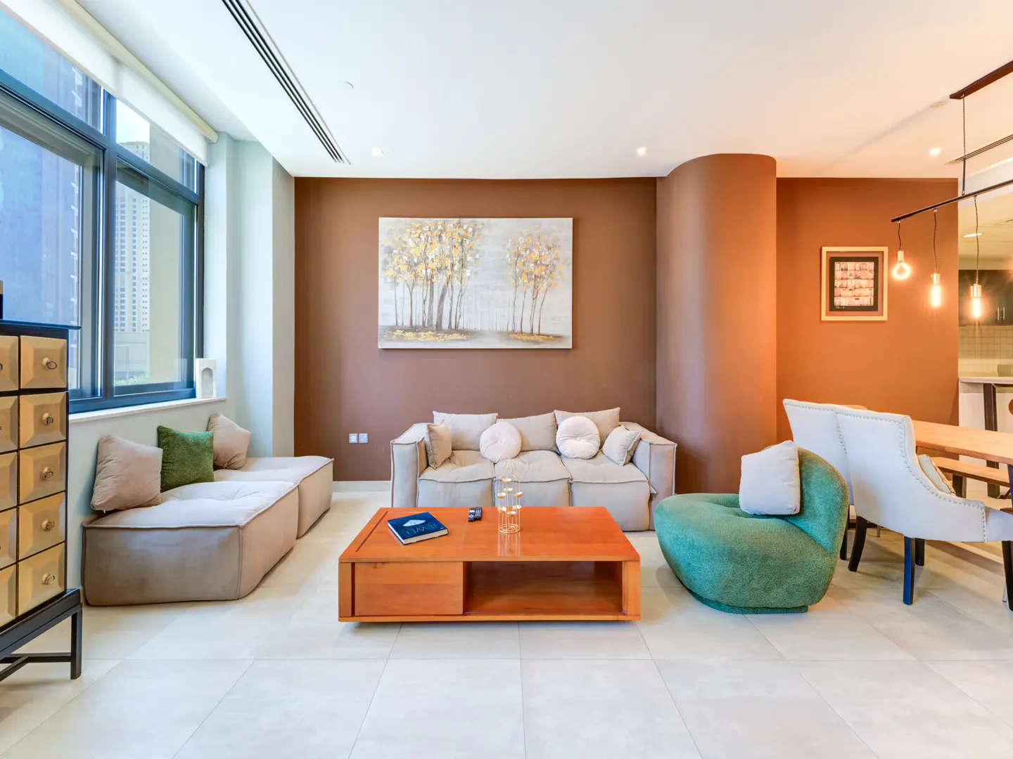 Living room with beige sofas, green chair, and orange coffee table on a white tile floor. A tree painting hangs on the brown wall.