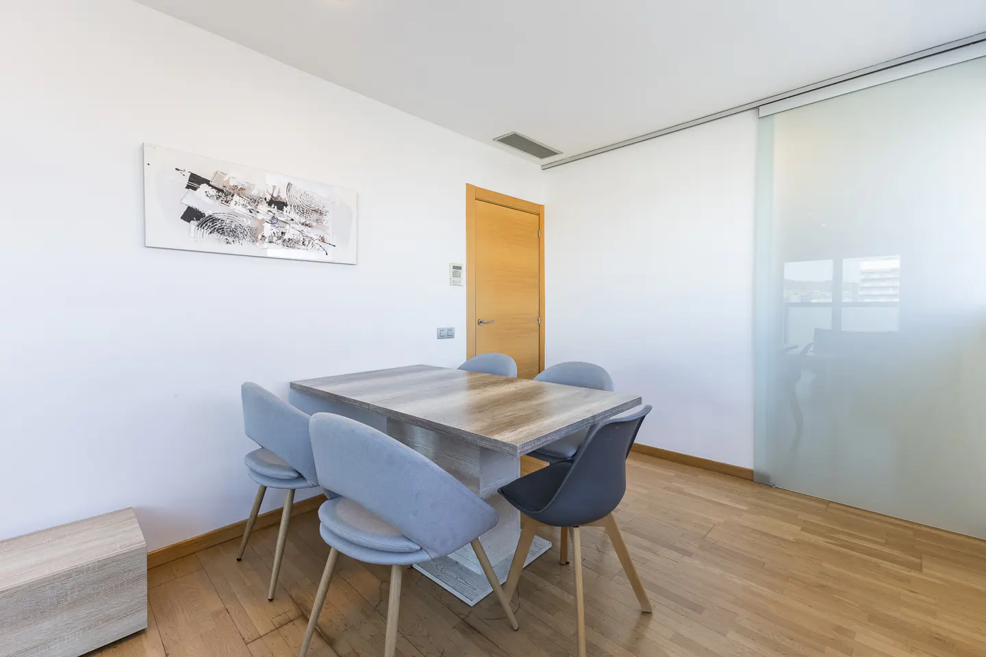 Dining area with a light wood table, four blue chairs, and a gray chair on a wood floor. A sliding glass door is on the right.