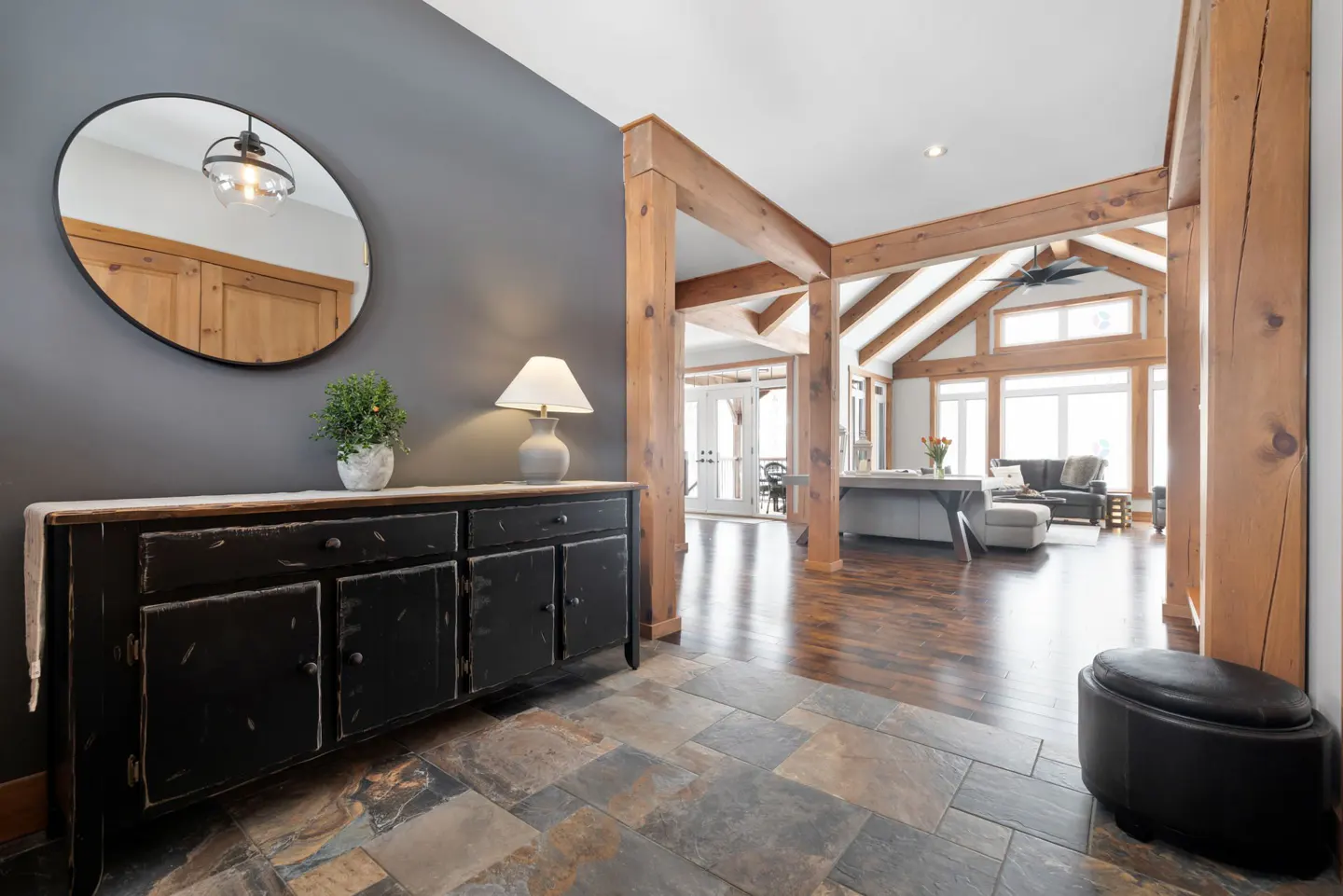 Interior view of a home's entryway with slate flooring, a black cabinet, and exposed wooden beams leading to a living area.