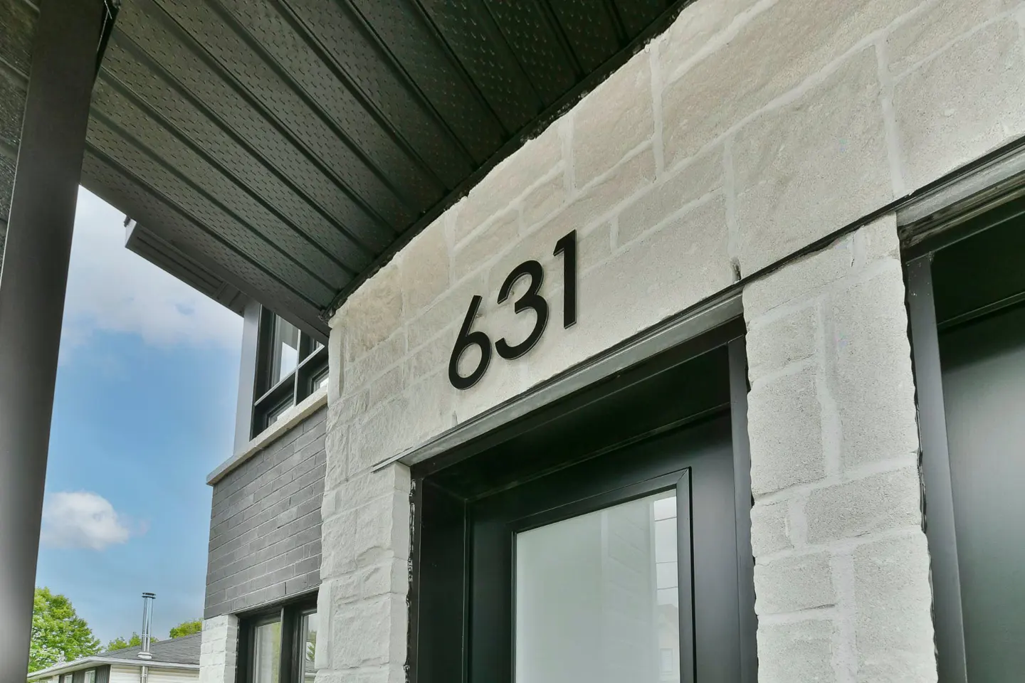 Close-up of a house entrance with the number 631 above a black door. The exterior is light stone with a dark metal awning.