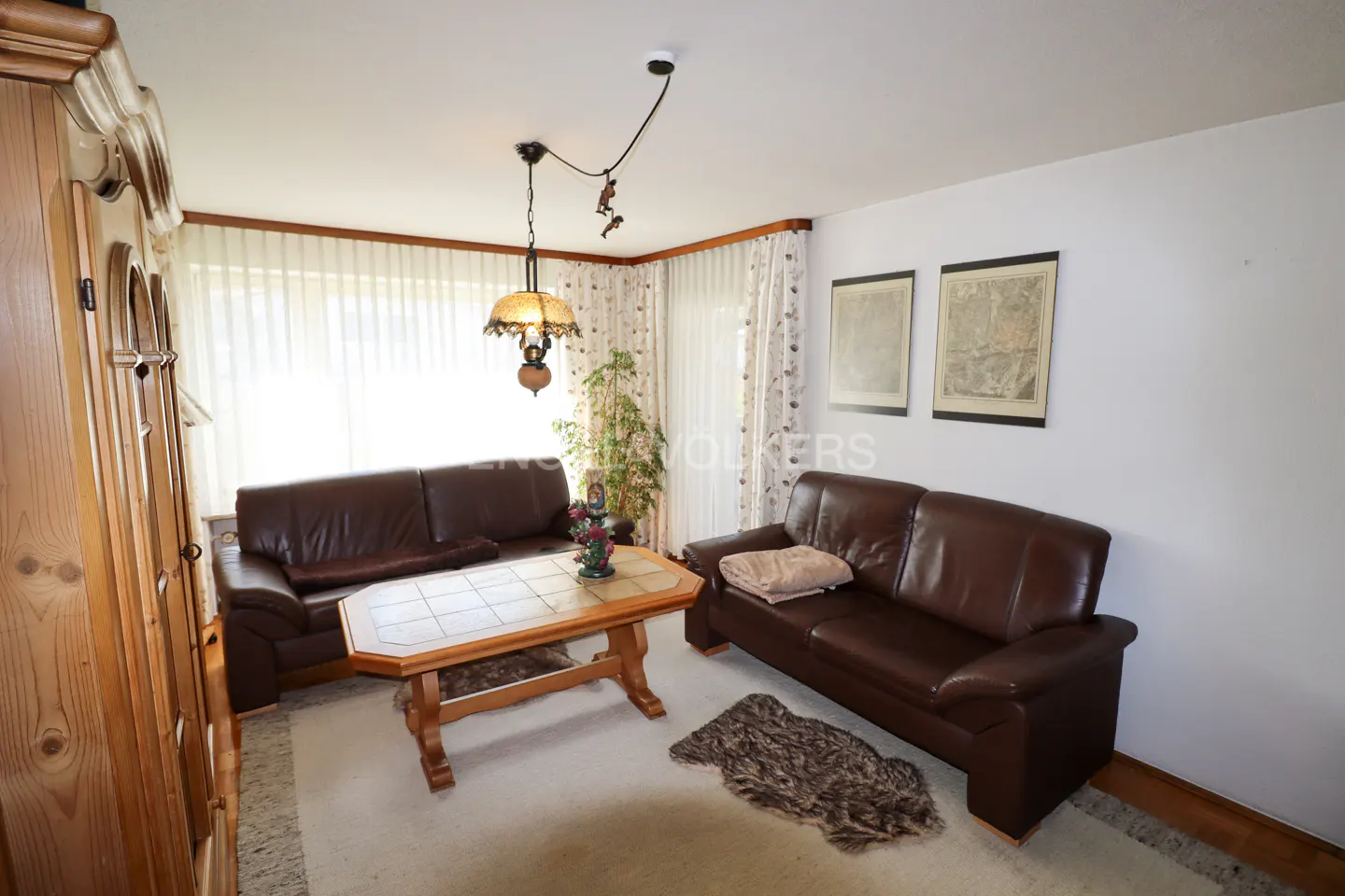 Living room with two brown leather sofas, a wooden coffee table, and a patterned rug on a light carpet. Two framed pictures hang on the wall.