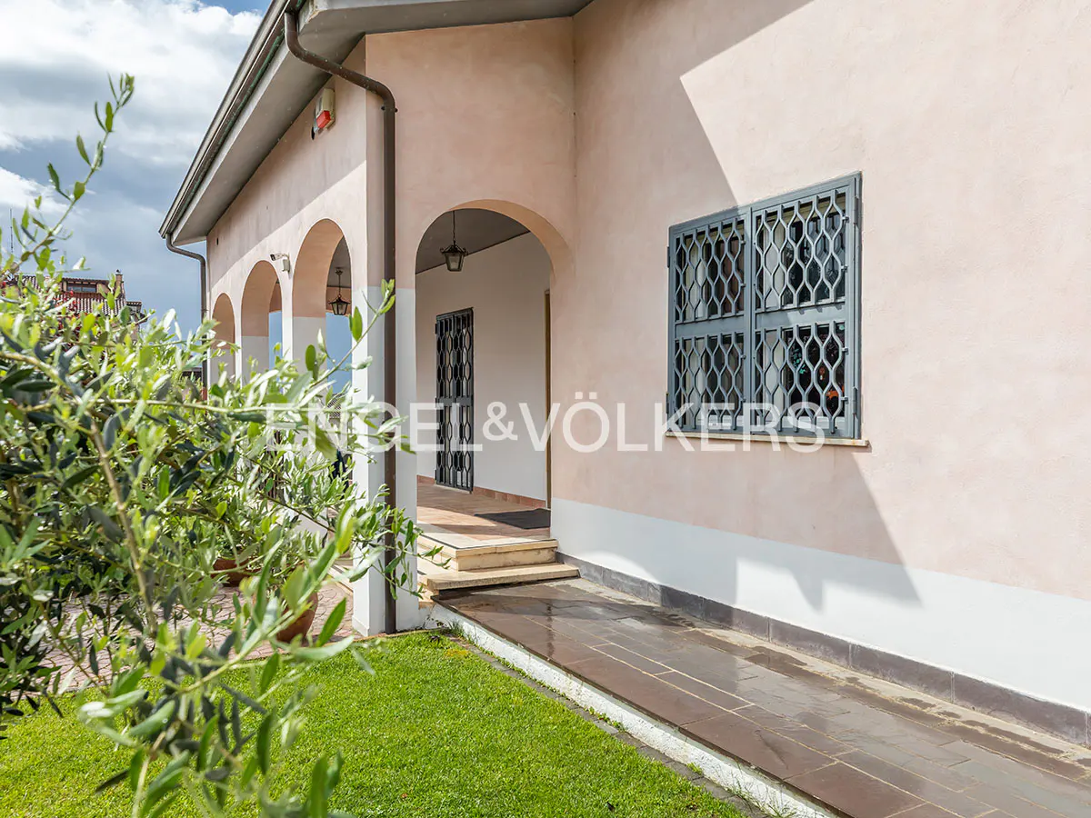 Exterior view of a pink stucco house with arched porch, gray window bars, and green lawn.