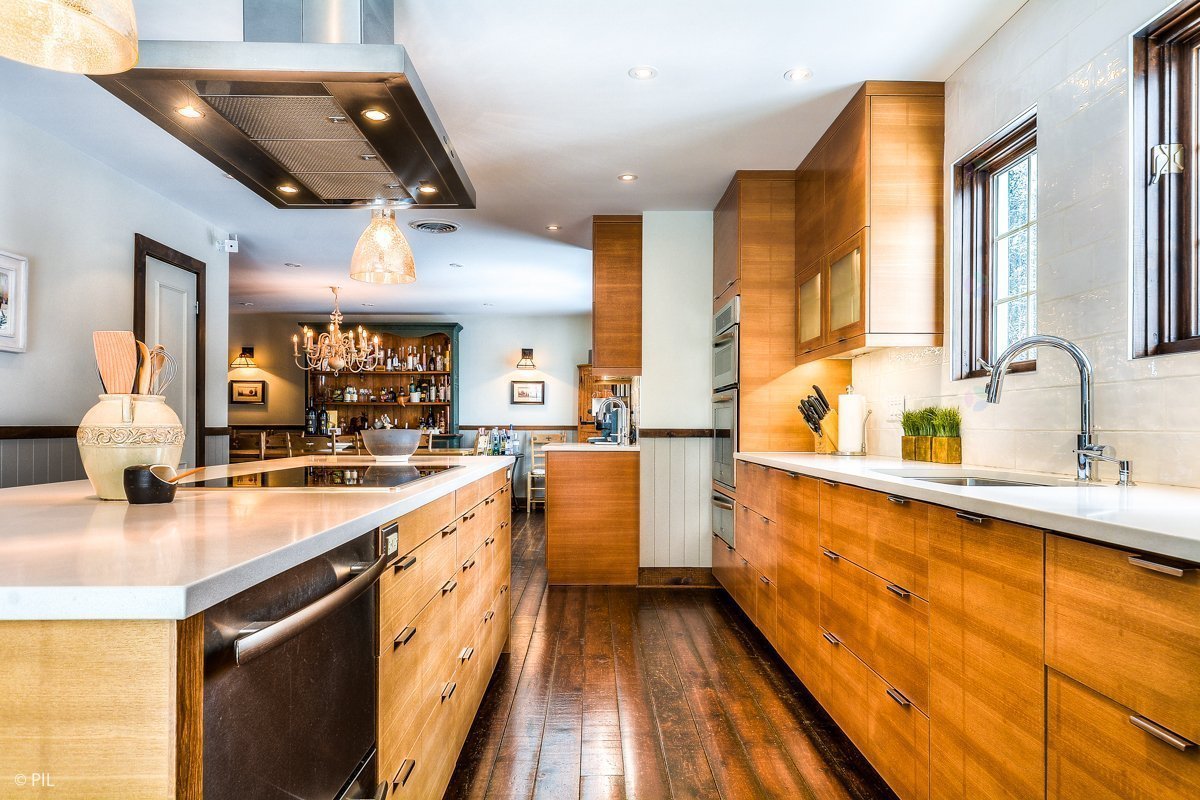 A bright kitchen with wood cabinets, white countertops, and dark wood floors. A large island sits in the center.