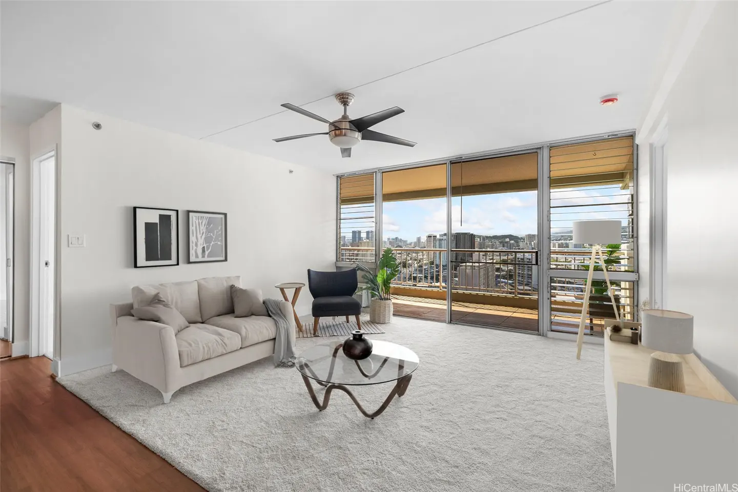 Modern living room with white sofa, glass coffee table, dark armchair, and floor-to-ceiling windows overlooking city view.
