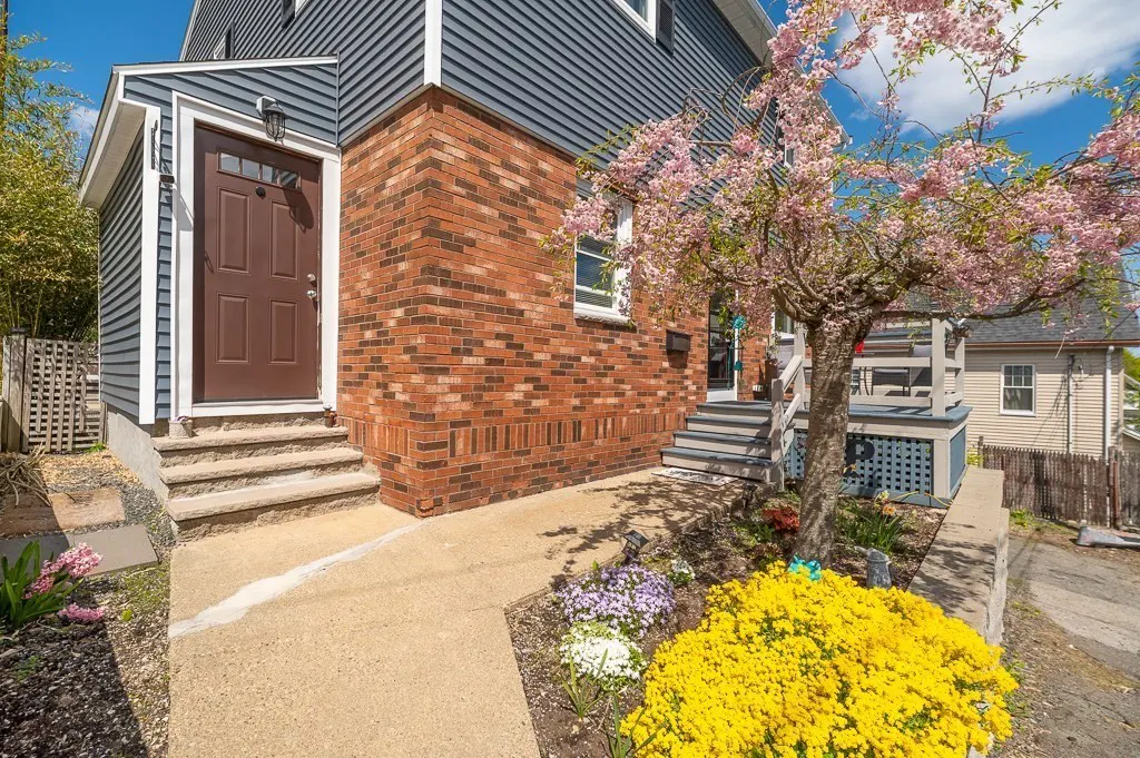 Exterior of a two-story house with blue siding, brick facade, brown door, and blooming cherry tree.