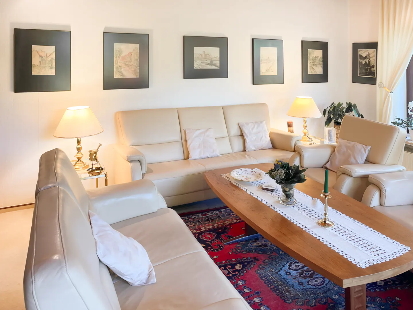 Living room with beige sofas, wooden table with white runner, and framed art on the wall. A patterned rug adds color to the space.
