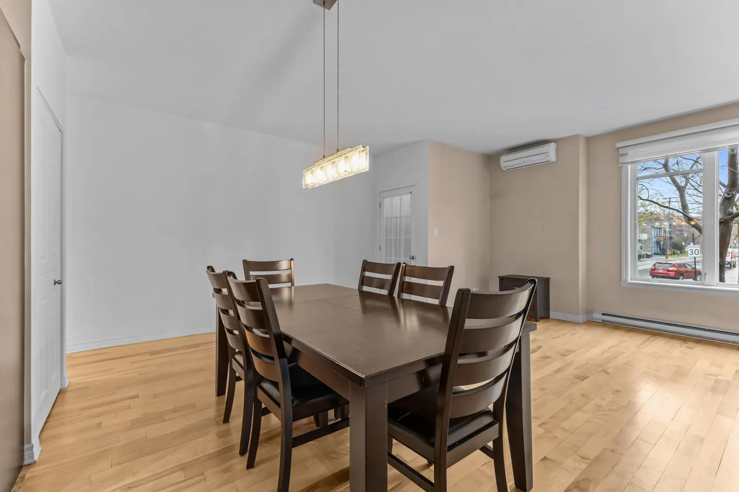 A dining room with a dark wood table and chairs, light wood floors, and a window.