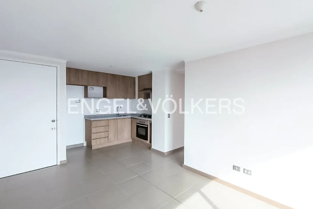 Modern kitchen with light wood cabinets, grey countertops, and tile flooring in an open-plan apartment.