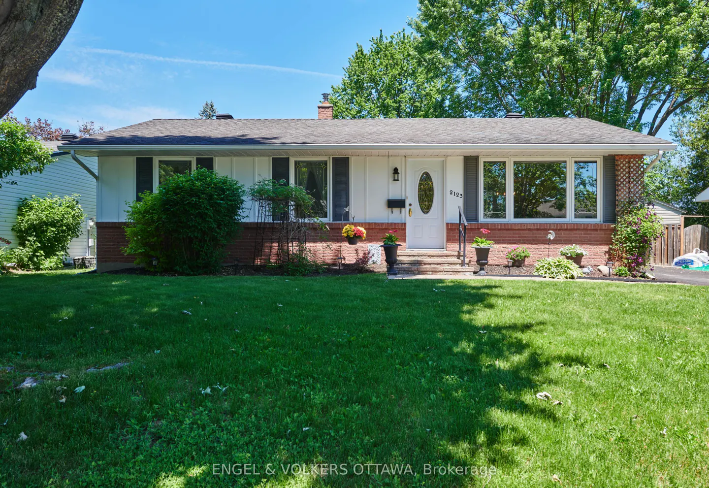 Single-story bungalow with white siding, red brick base, and a green lawn under a clear blue sky.
