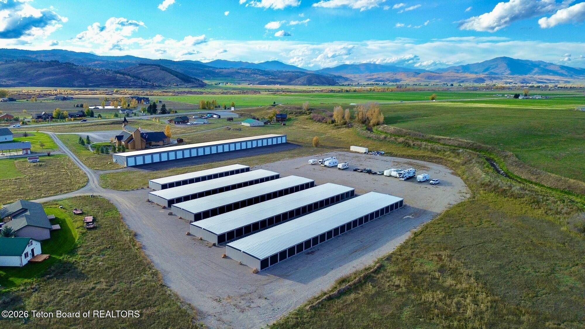 Aerial view of a self-storage facility with multiple long white buildings on a gravel lot, set against a mountain landscape. [AI-generated text]