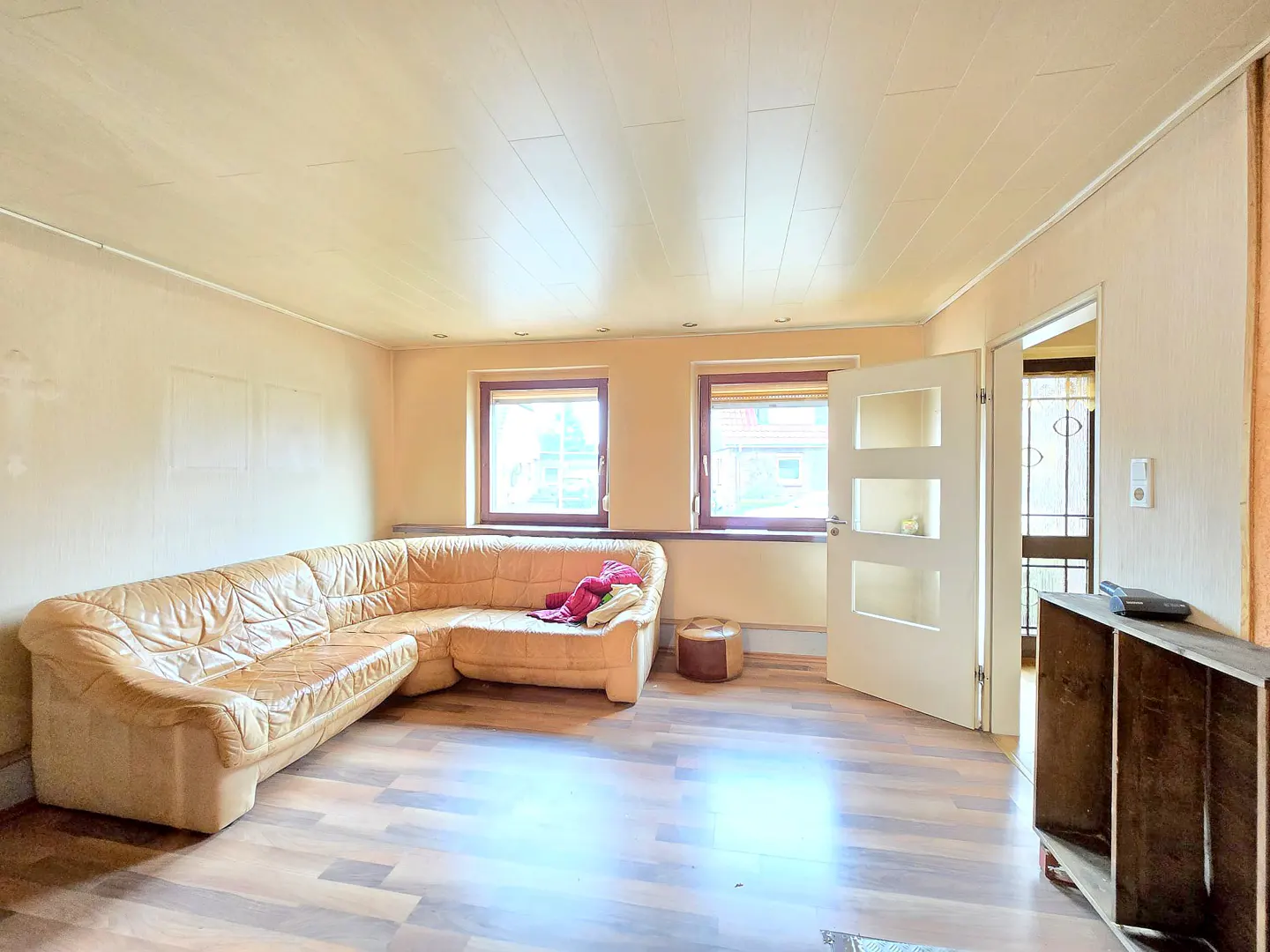 Living room with a tan leather sectional sofa, wood floors, two windows, and a white door ajar.