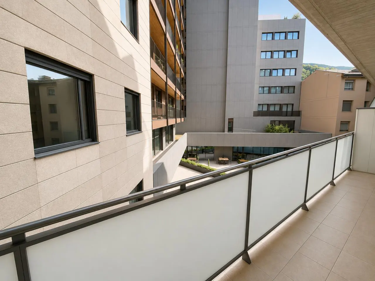 View from a balcony with a metal railing, overlooking a courtyard with buildings in the background.