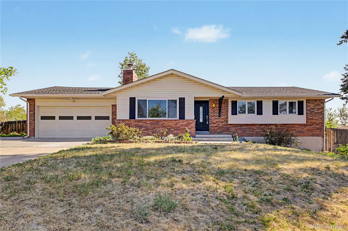 A ranch-style home with a brick facade, white siding, and a two-car garage under a blue sky.