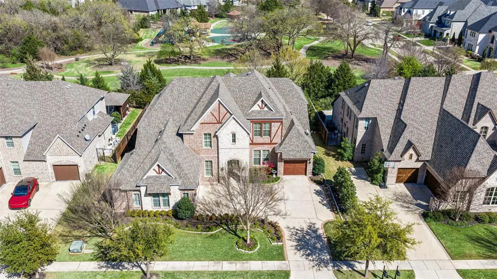 Aerial view of a large, two-story brick home with a gray roof, surrounded by green lawns and trees in a suburban neighborhood.