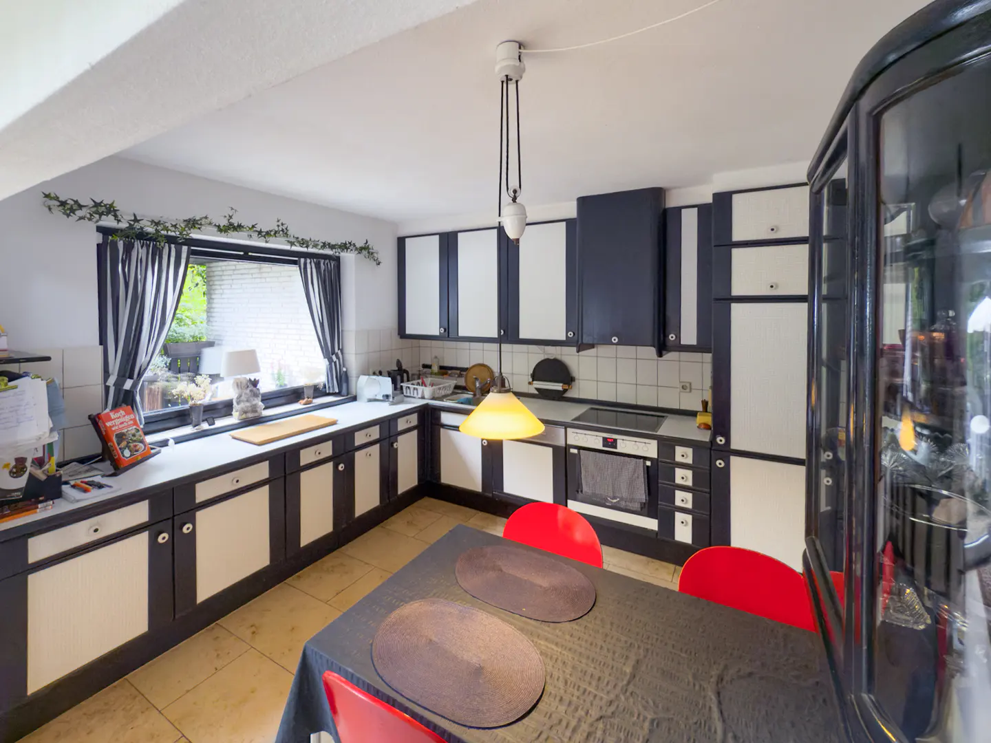 A kitchen with black and white cabinets, a black table with red chairs, and a window with striped curtains.