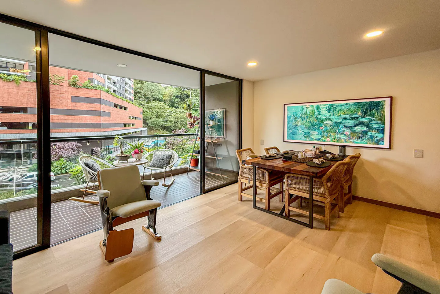Dining area with wooden table and chairs, large impressionist art, and a balcony with outdoor seating and city views.