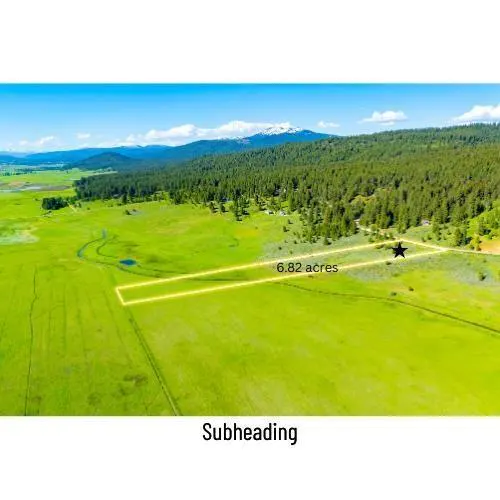 Aerial view of a 6.82-acre plot of green land outlined in yellow, set against a backdrop of forest and distant mountains.