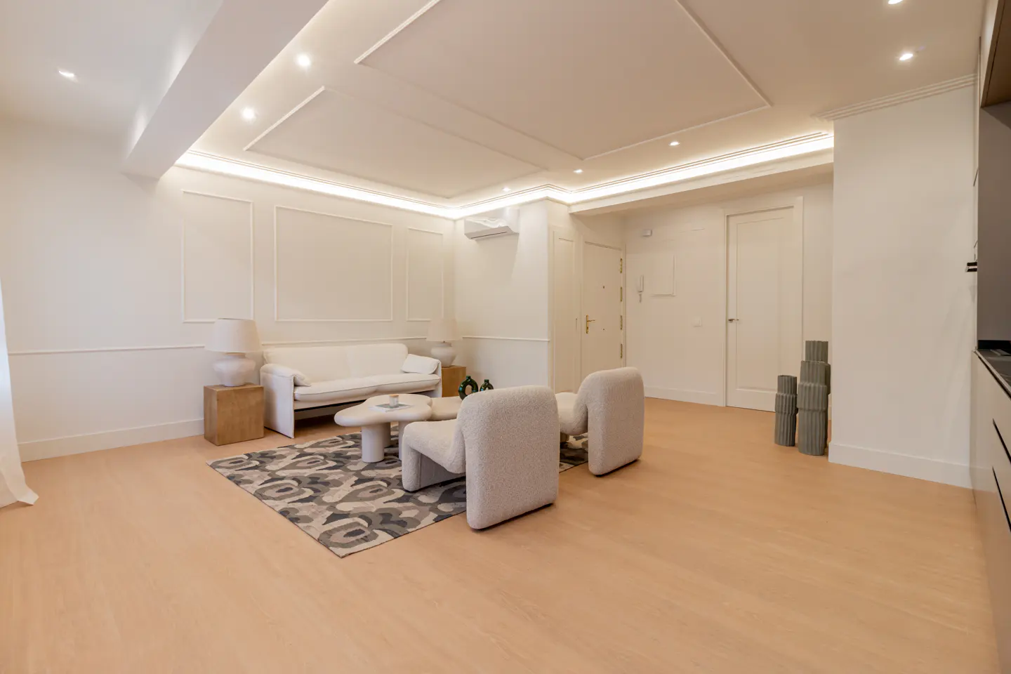 Modern living room with white walls, light wood floors, a white sofa, two armchairs, and a patterned rug.