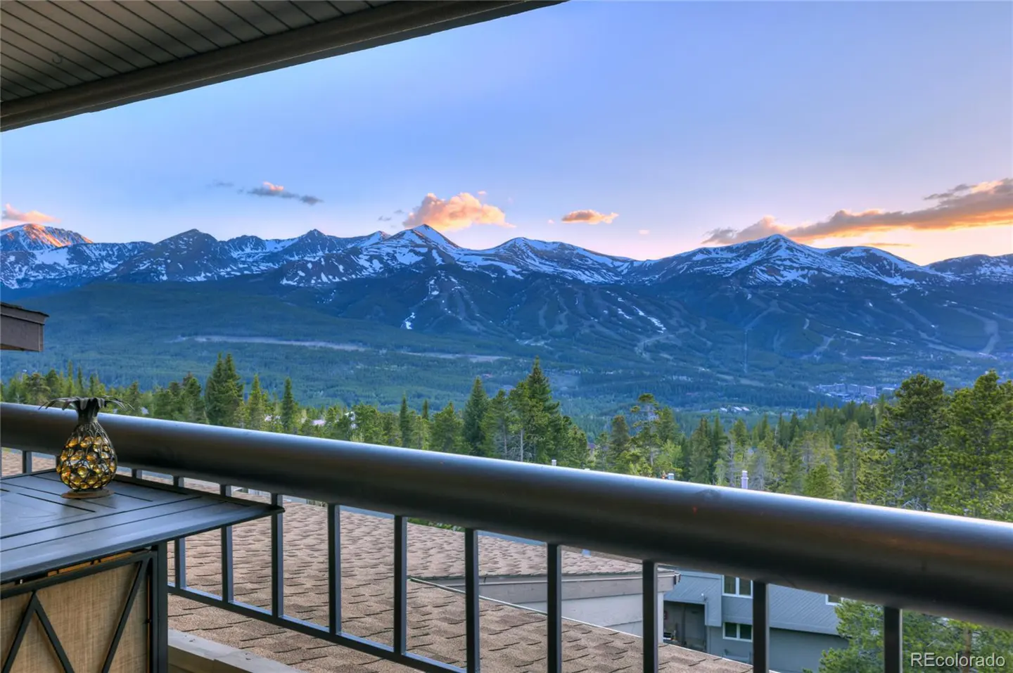Balcony view of snow-capped mountains at sunset with a pineapple-shaped lantern on a table in the foreground.