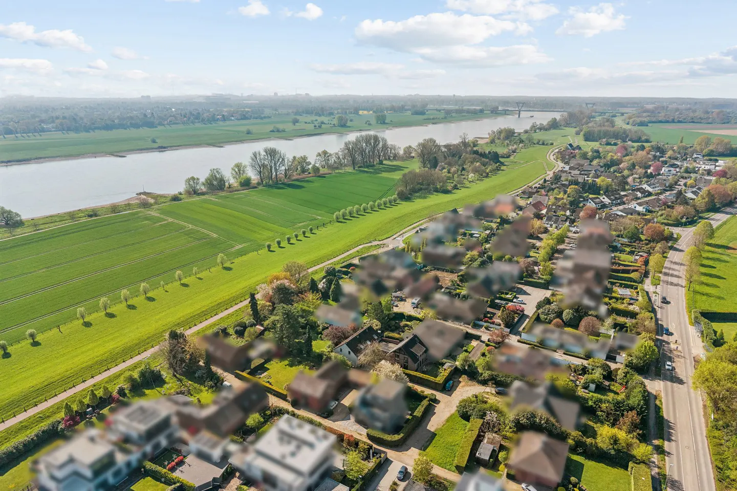 Aerial view of a neighborhood with green fields, a river, and a blue sky.
