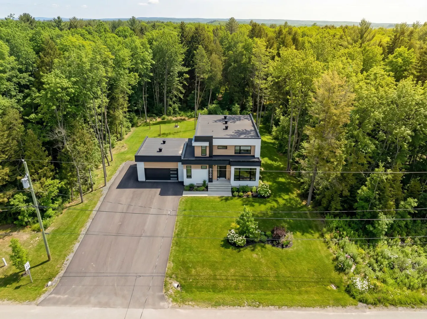 Aerial view of a modern two-story house with a flat roof, a garage, and a green lawn surrounded by trees.