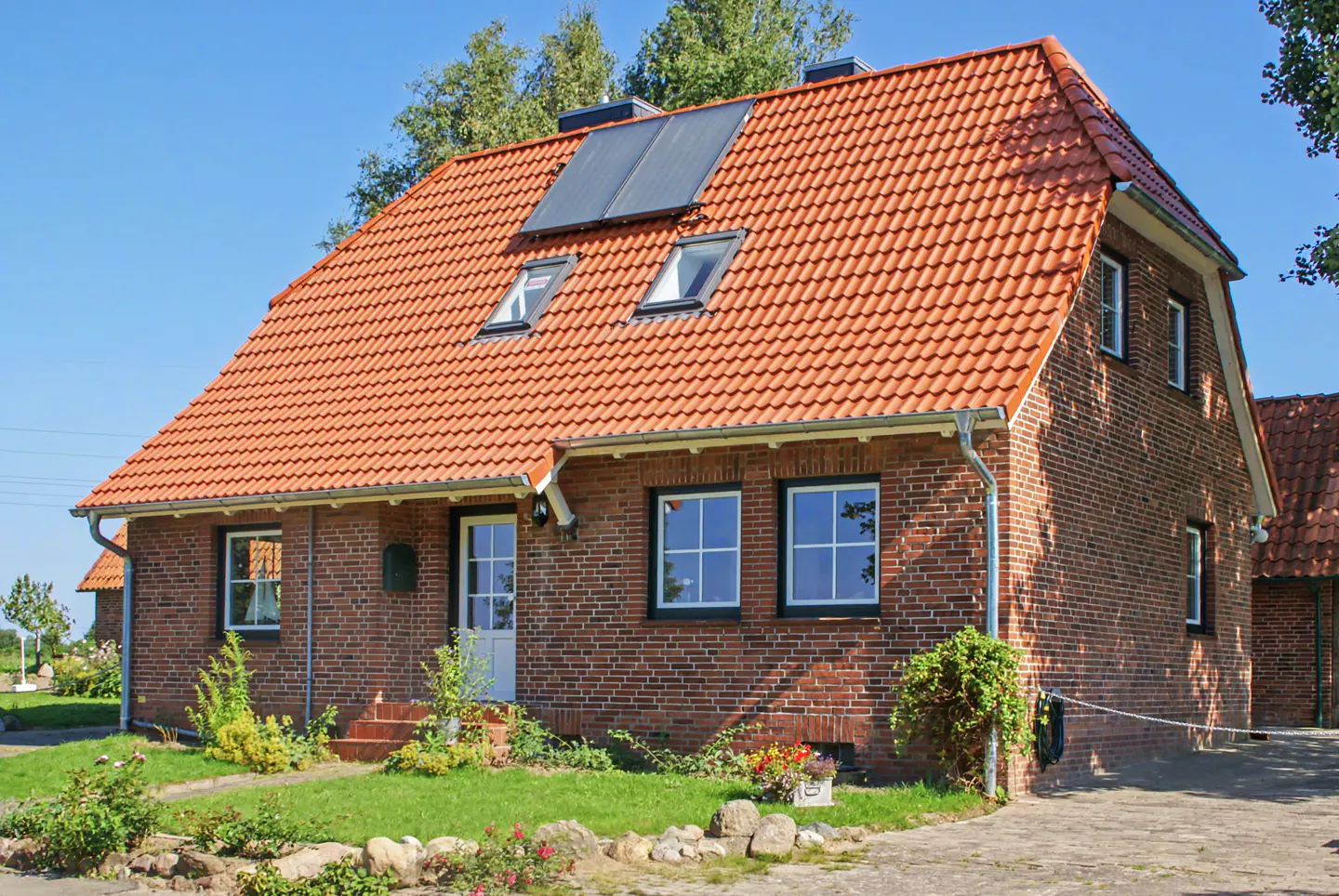 A two-story brick house with a red tile roof, solar panels, and a green lawn on a sunny day.