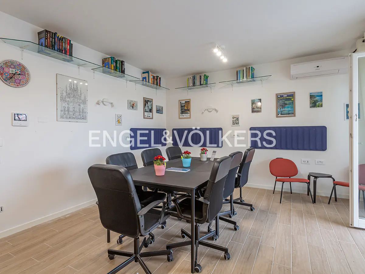 Bright office space with a black conference table, rolling chairs, and wall-mounted bookshelves. Red flowers add a pop of color.