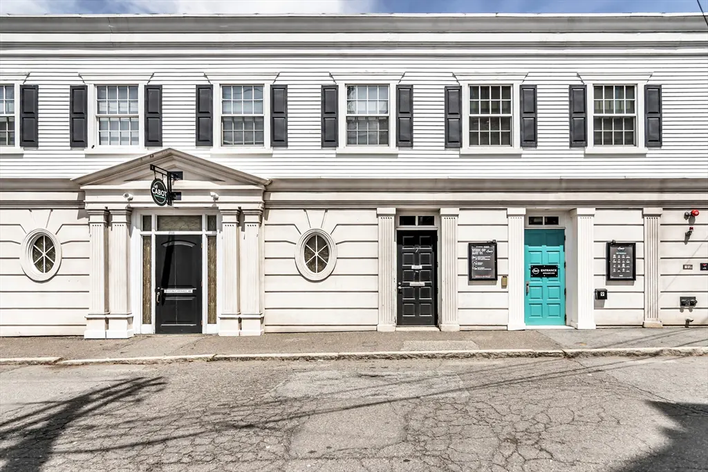 Exterior of a white building with black shutters and three doors, one turquoise.