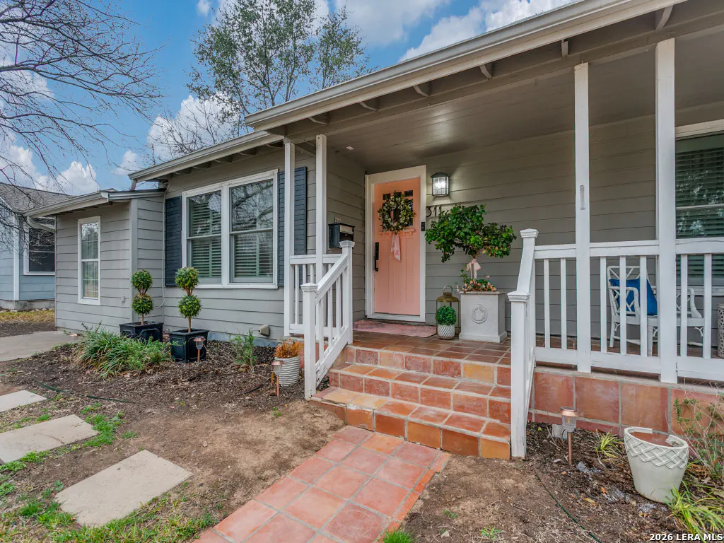 Exterior view of a gray house with a pink front door, white porch railing, and brick steps.
