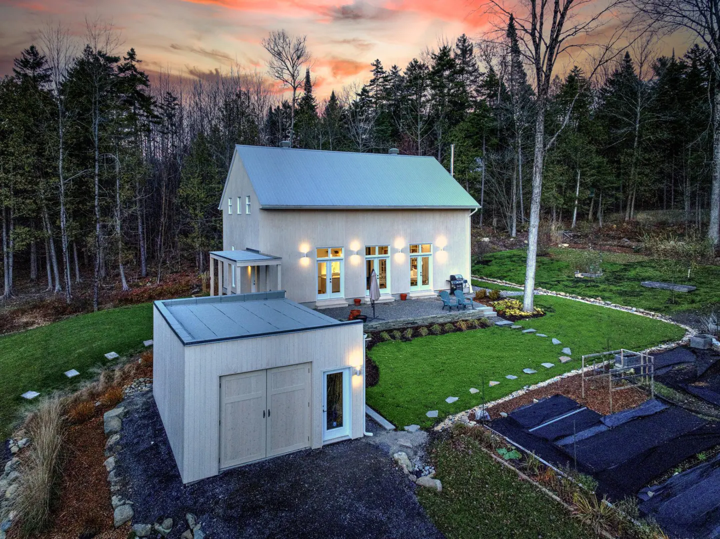 Exterior view of a modern farmhouse with a metal roof, a detached garage, and a lush green lawn.