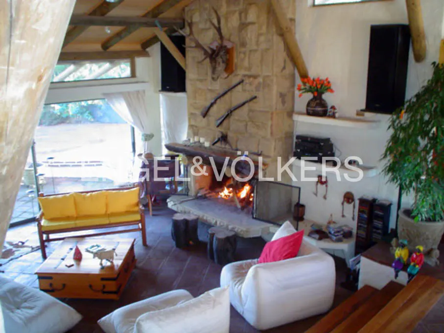 Living room with stone fireplace, mounted deer head, and decorative rifles. Yellow sofa, white chairs, and wood accents.