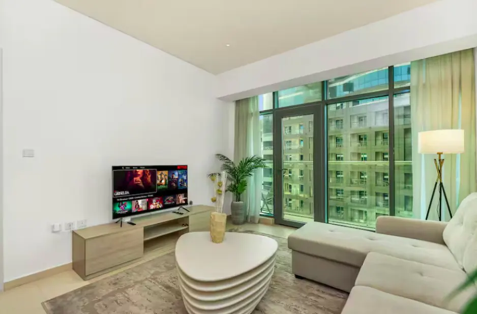 Living room with a beige sectional sofa, TV, and a large window showing a city view.