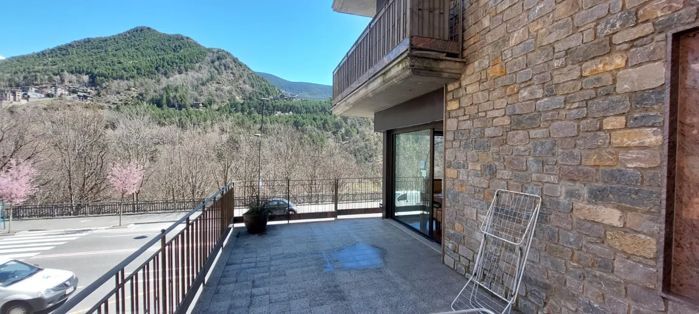 Balcony view of a stone building with a mountain backdrop. A clothes drying rack stands against the stone wall.
