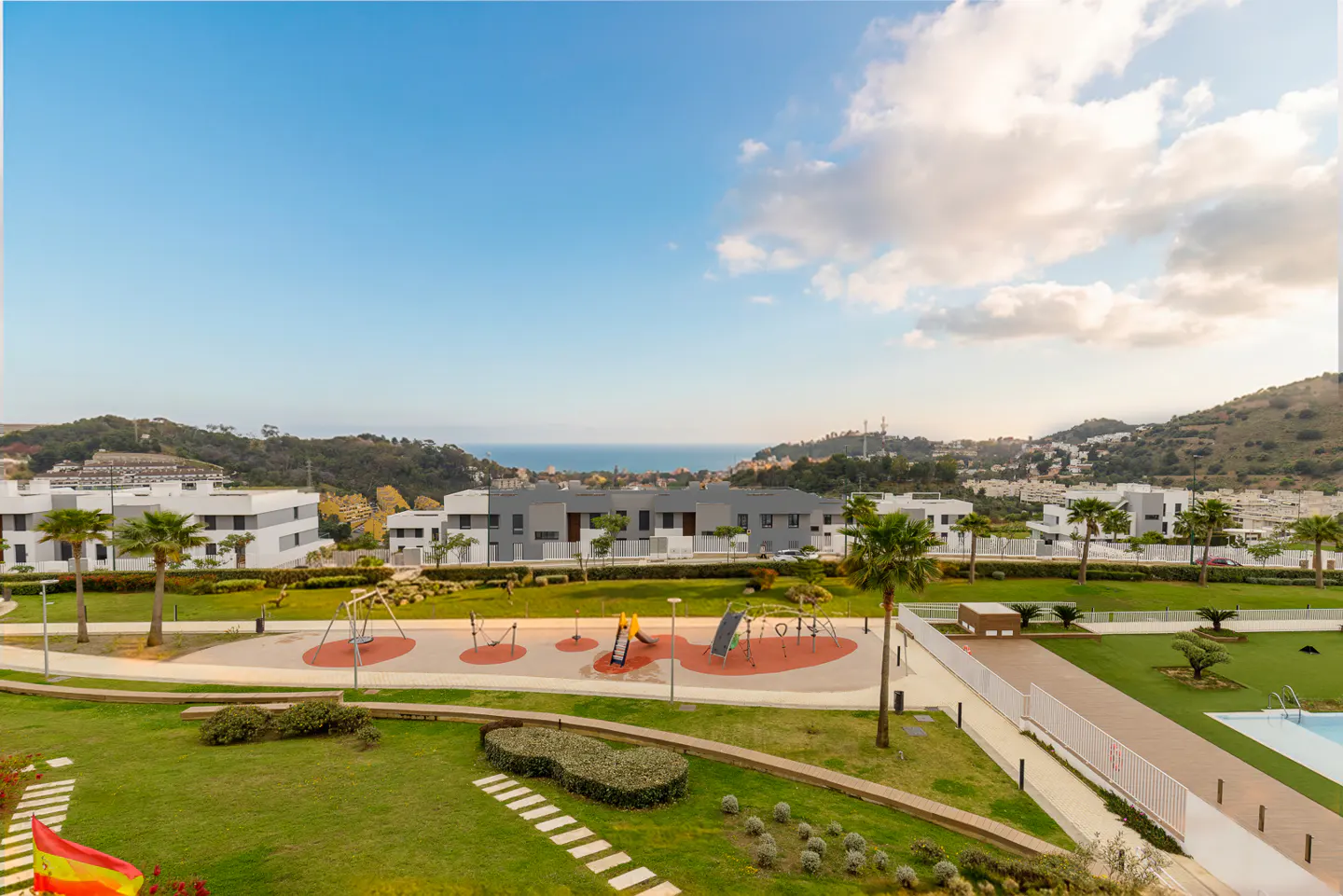View of modern white and gray townhouses with a playground, pool, and green space under a blue sky.