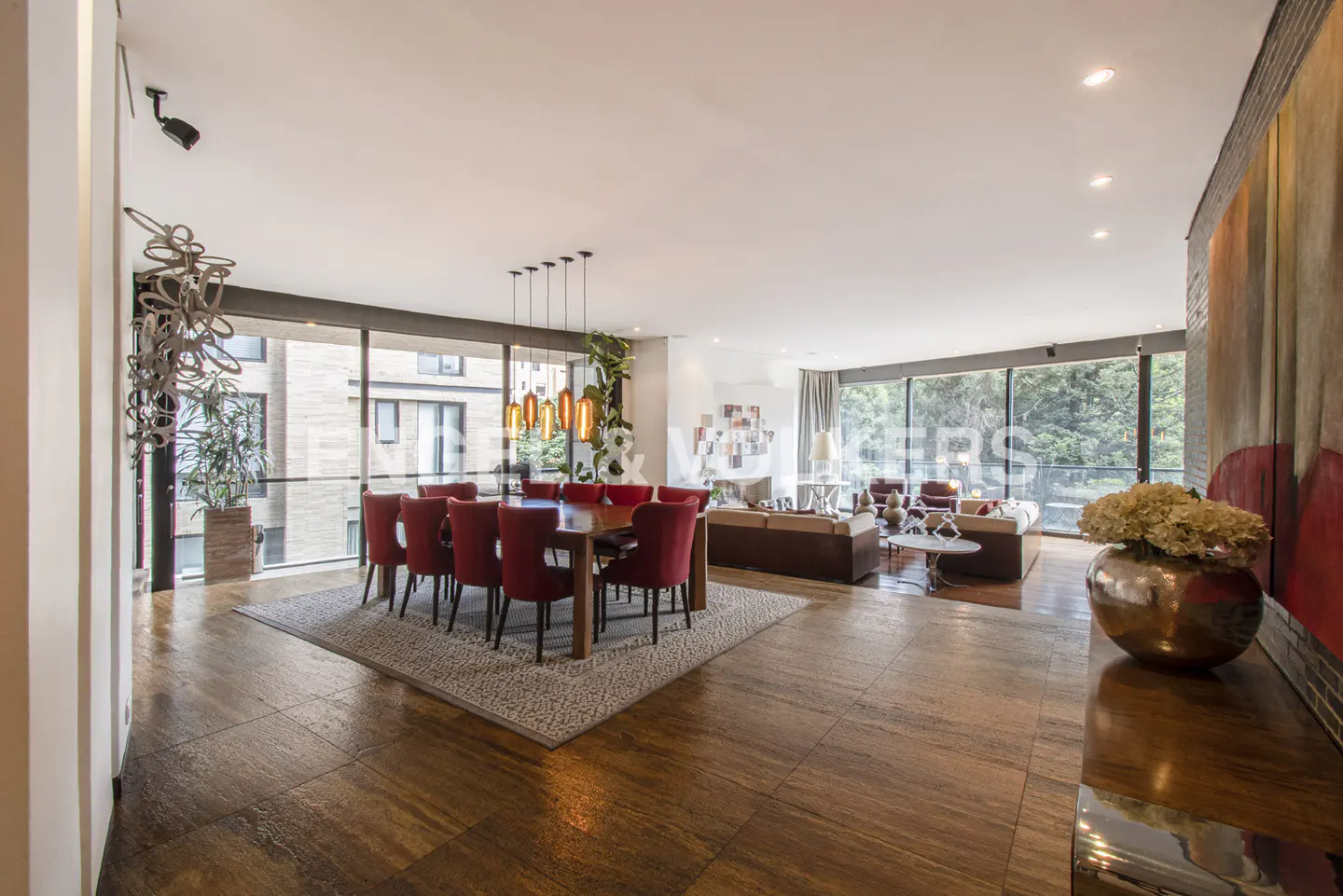 Open-concept living and dining area with wood floors, red chairs around a table, and floor-to-ceiling windows.