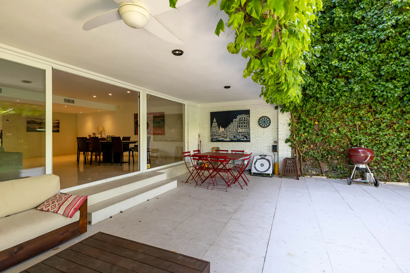 Outdoor patio with red table and chairs, grill, and ivy-covered wall. Sliding glass doors lead to a dining room.