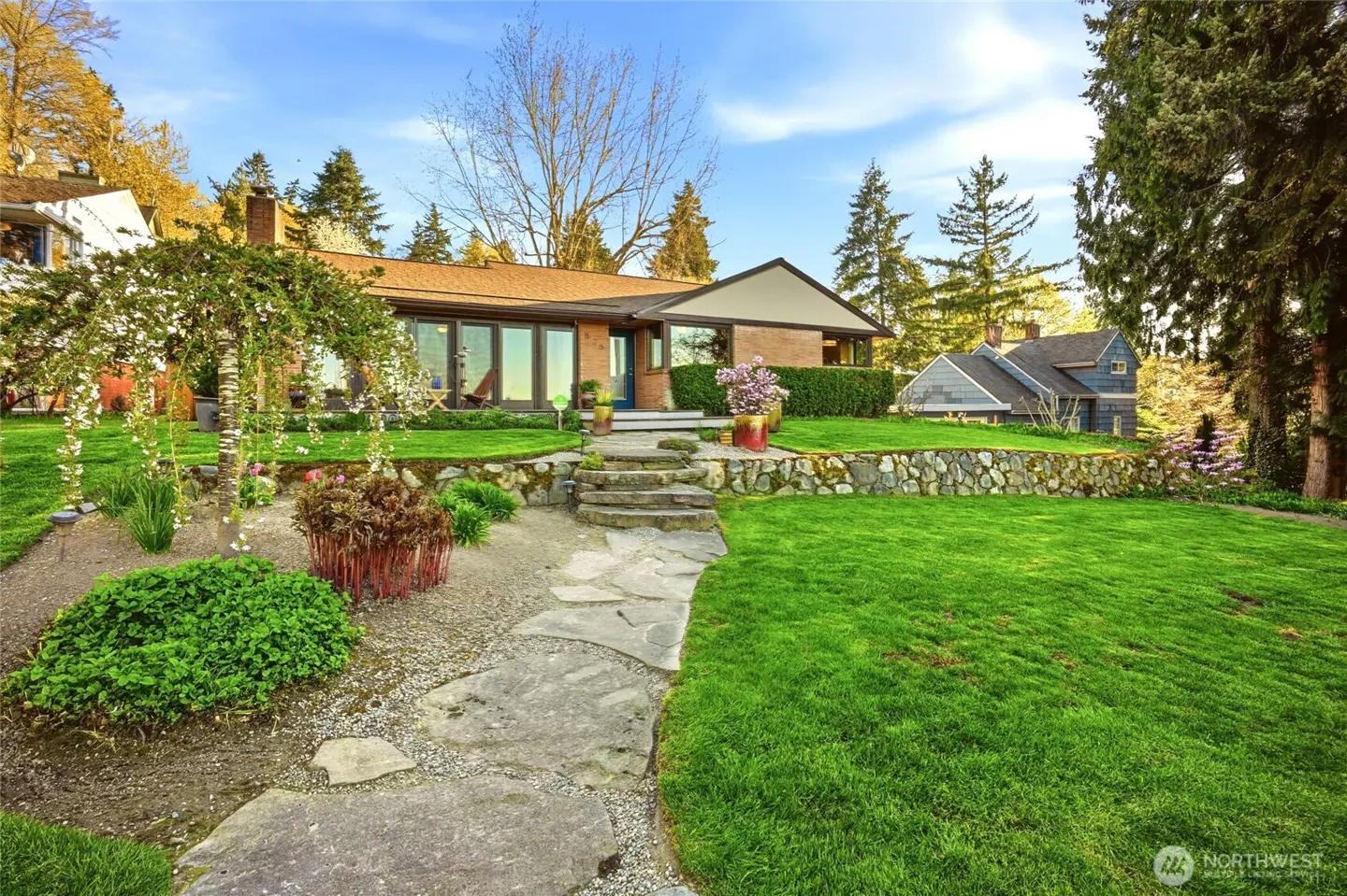 A single-story brick house with a stone walkway and green lawn under a blue sky.
