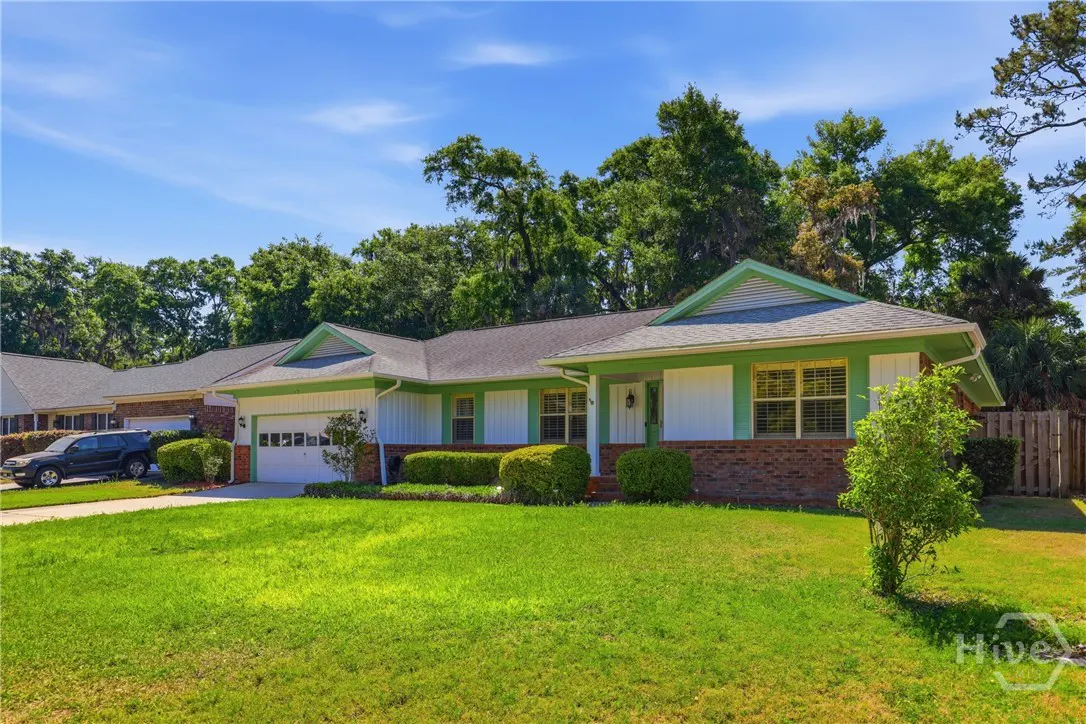 A ranch-style house with green trim, white siding, and a brick facade sits on a green lawn under a blue sky.